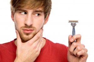 A young man rubbing his beard and looking at his razor.