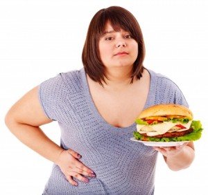 a fat girl holding her side with one hand and a plate filled with food in the other hand